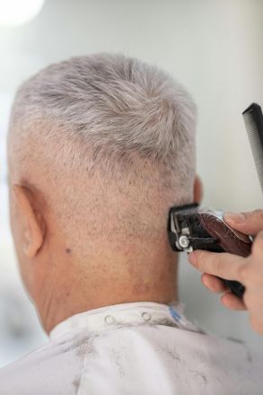 Elderly man getting hair trimmed by barber indoors using clipper and comb.