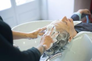 Close-up of senior woman getting hair washed with foam at salon sink, enjoying the pampering session.